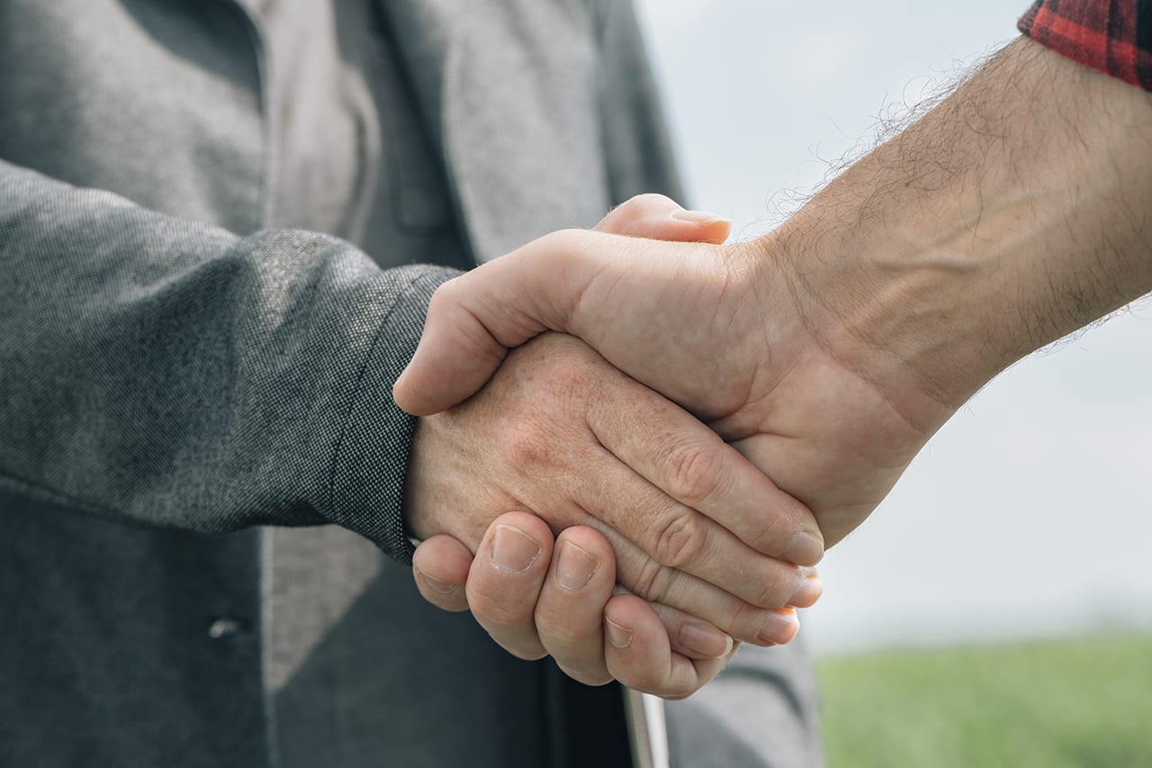 Mortgage loan officer and farmer shaking hands upon reaching an
