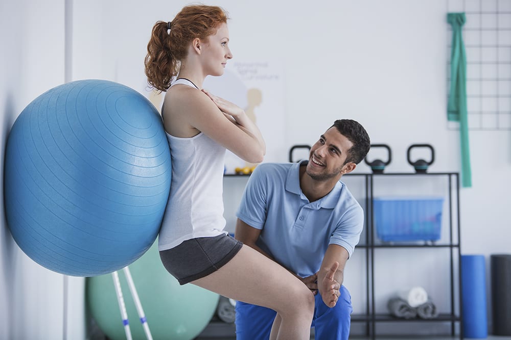 Smiling professional personal trainer helping sportswoman exerci